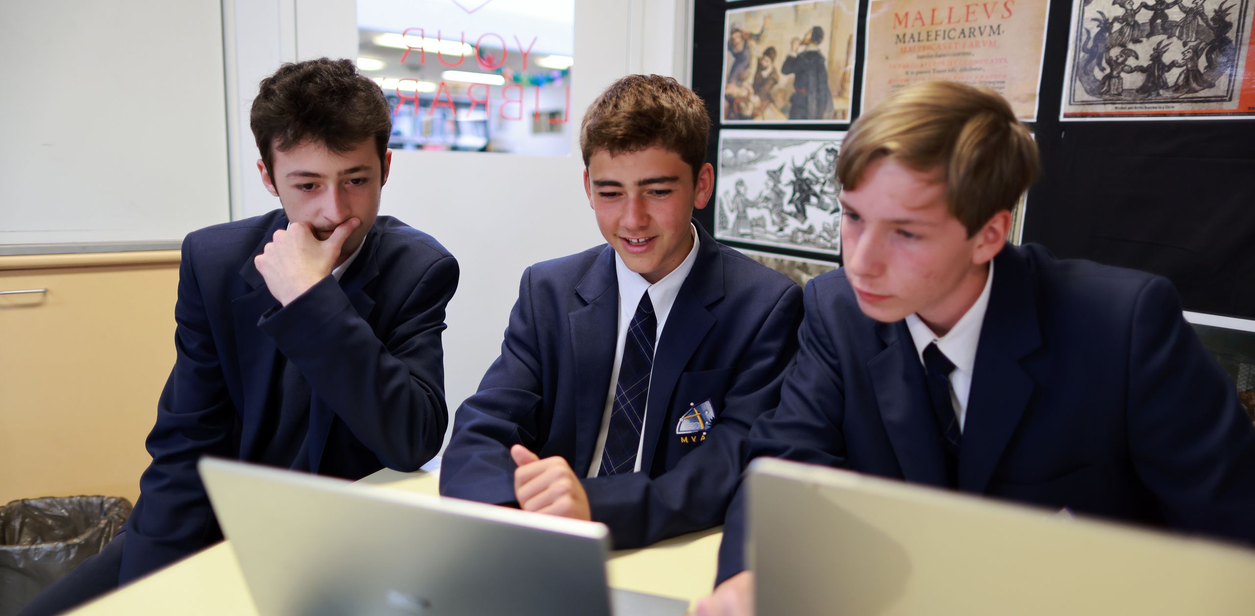 Three senior students wearing the college navy blazer looking at their computers during a history lesson.
